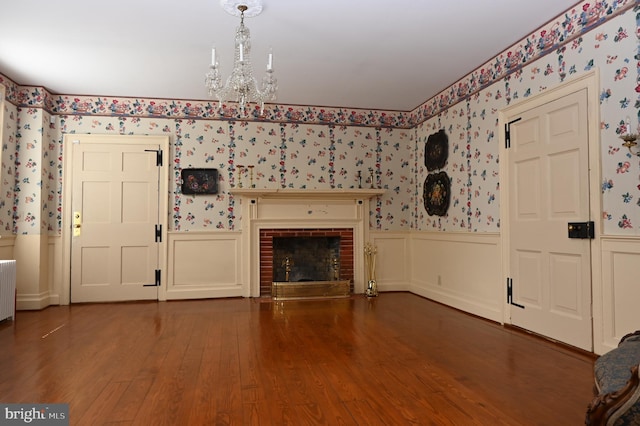 unfurnished living room featuring a brick fireplace, a chandelier, radiator, and dark hardwood / wood-style flooring