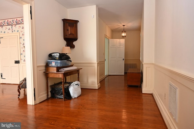 corridor with dark wood-type flooring, radiator heating unit, and a chandelier