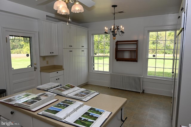 kitchen with white cabinetry, decorative light fixtures, radiator heating unit, and ceiling fan with notable chandelier