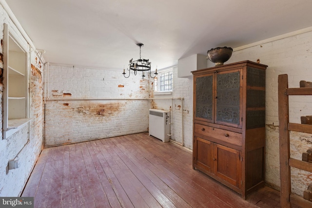 unfurnished dining area featuring a notable chandelier, hardwood / wood-style flooring, and brick wall