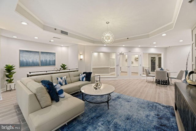 living room with french doors, a notable chandelier, a tray ceiling, and light wood-type flooring