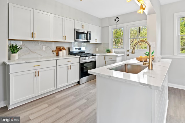 kitchen featuring backsplash, appliances with stainless steel finishes, white cabinetry, light wood-type flooring, and sink