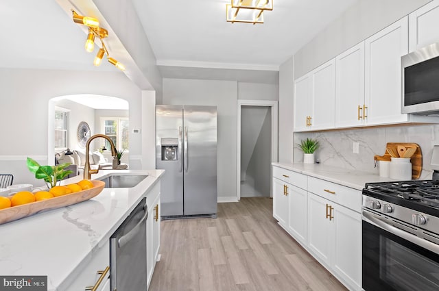 kitchen featuring sink, white cabinetry, light wood-type flooring, appliances with stainless steel finishes, and light stone counters