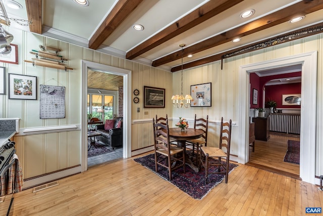 dining room featuring beamed ceiling, wooden walls, and light hardwood / wood-style flooring