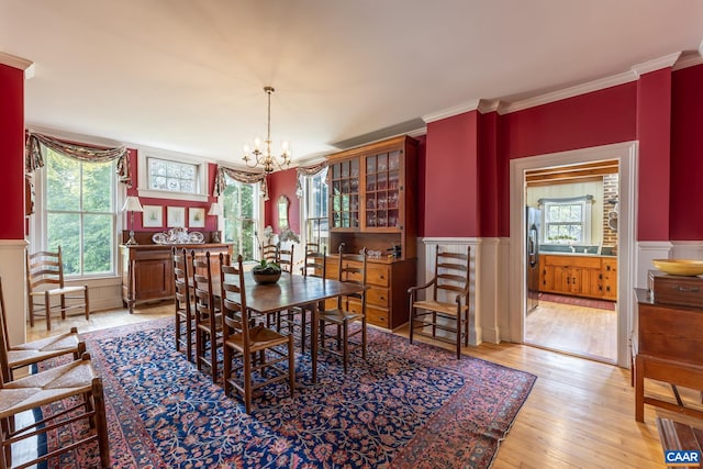 dining space with light wood-type flooring, crown molding, an inviting chandelier, and plenty of natural light