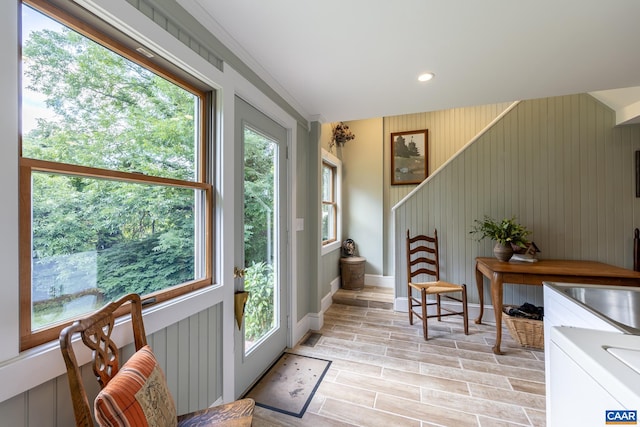 doorway to outside featuring light hardwood / wood-style floors, crown molding, wood walls, and plenty of natural light