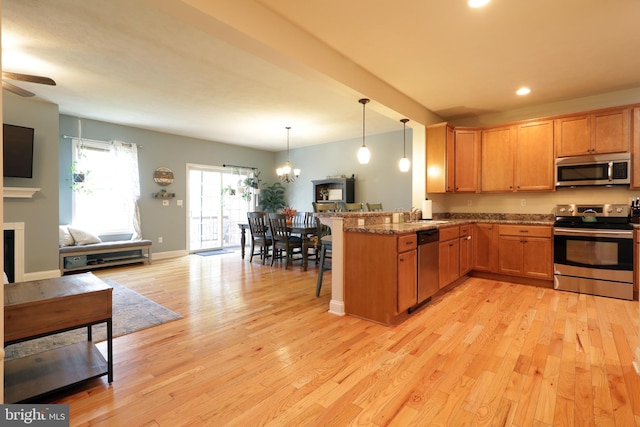 kitchen with light hardwood / wood-style flooring, kitchen peninsula, stainless steel appliances, light stone countertops, and decorative light fixtures