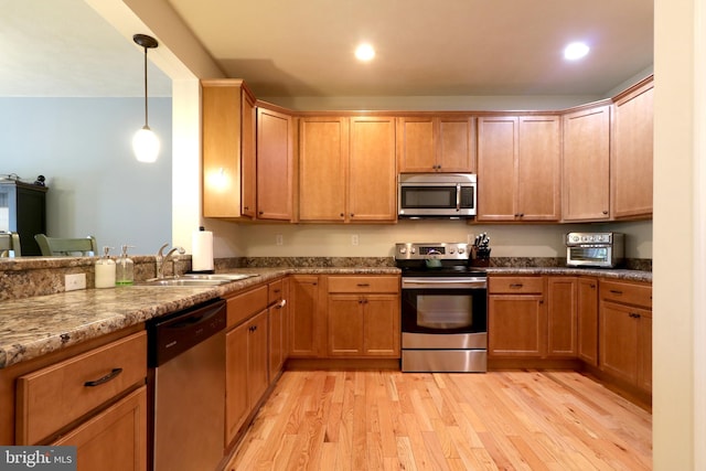 kitchen with hanging light fixtures, stainless steel appliances, sink, light wood-type flooring, and stone counters