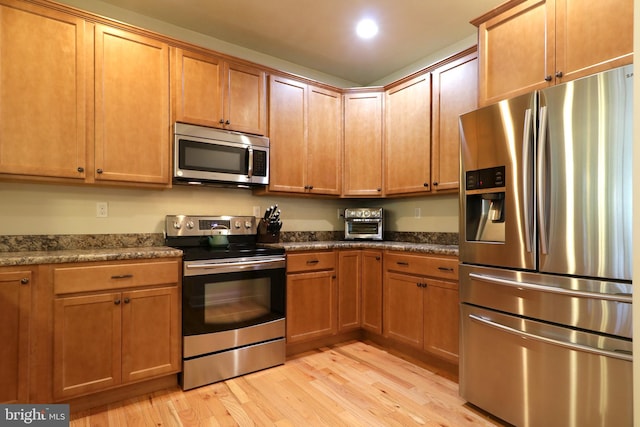 kitchen with dark stone countertops, appliances with stainless steel finishes, and light wood-type flooring