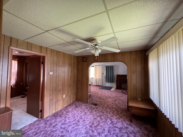 interior space featuring a drop ceiling, wood walls, and carpet