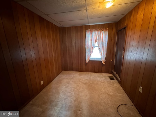 unfurnished room with wood walls, a paneled ceiling, and carpet