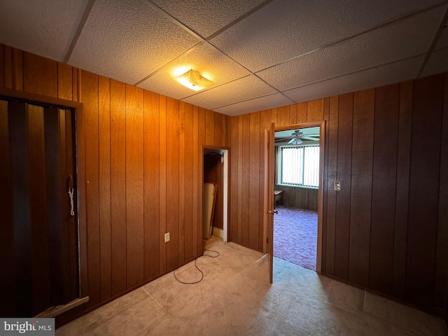 spare room featuring ceiling fan, wood walls, a paneled ceiling, and light colored carpet