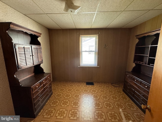 interior space with a drop ceiling and wood walls