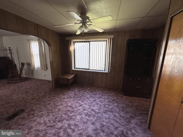 carpeted spare room featuring wooden walls, a drop ceiling, and ceiling fan