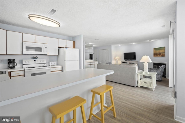 kitchen featuring white cabinets, a textured ceiling, a kitchen bar, light hardwood / wood-style floors, and white appliances