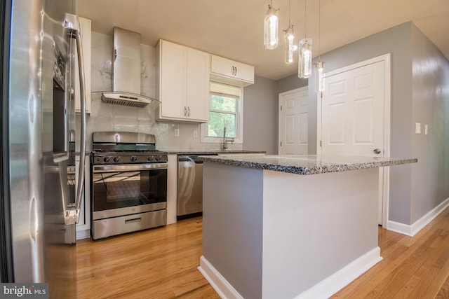 kitchen with wall chimney range hood, stainless steel appliances, a center island, white cabinetry, and light hardwood / wood-style floors