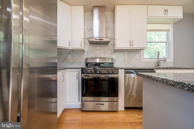 kitchen featuring white cabinetry, wall chimney range hood, appliances with stainless steel finishes, and light wood-type flooring