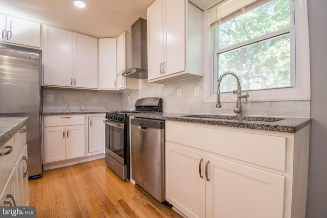 kitchen with appliances with stainless steel finishes, wall chimney exhaust hood, white cabinets, and sink