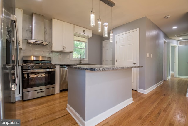 kitchen with wall chimney range hood, white cabinetry, light hardwood / wood-style flooring, stainless steel appliances, and a center island