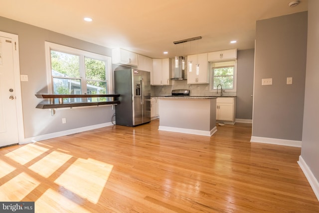 kitchen featuring white cabinets, stainless steel appliances, pendant lighting, wall chimney exhaust hood, and a center island