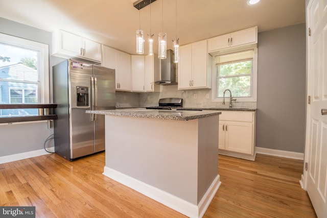 kitchen featuring appliances with stainless steel finishes, a kitchen island, white cabinetry, light hardwood / wood-style floors, and wall chimney exhaust hood