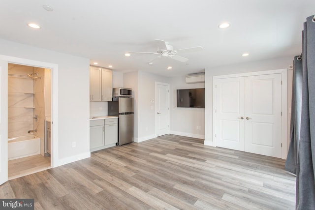 kitchen with an AC wall unit, appliances with stainless steel finishes, light hardwood / wood-style floors, and ceiling fan