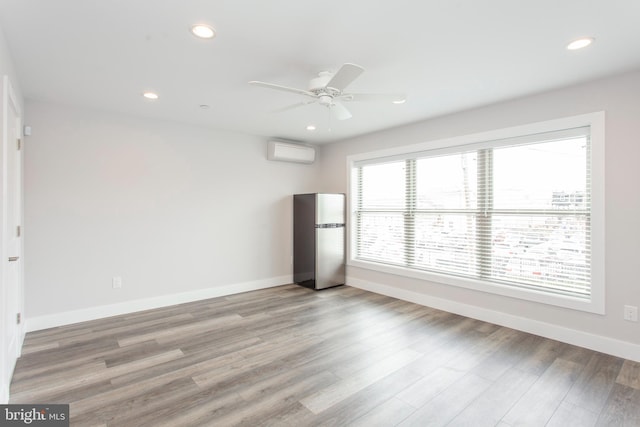 empty room featuring ceiling fan, an AC wall unit, and light hardwood / wood-style flooring