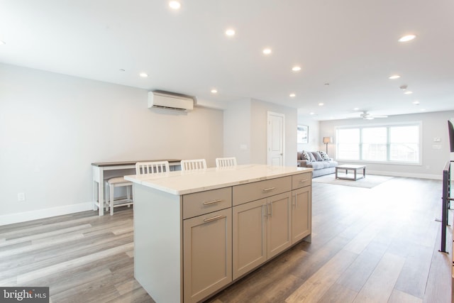 kitchen with light wood-type flooring, an AC wall unit, a center island, a kitchen breakfast bar, and ceiling fan