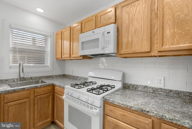 kitchen with white appliances, backsplash, sink, and light stone counters