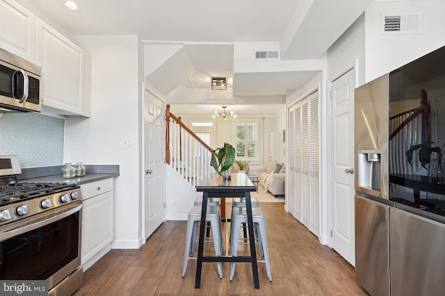 kitchen featuring decorative backsplash, hardwood / wood-style flooring, a notable chandelier, white cabinetry, and appliances with stainless steel finishes