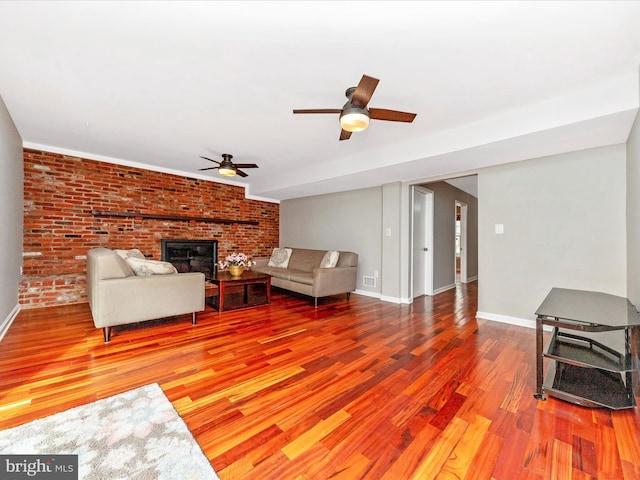 living room featuring hardwood / wood-style floors, ceiling fan, brick wall, and a brick fireplace