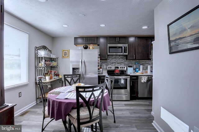 kitchen featuring dark brown cabinets, backsplash, a textured ceiling, light hardwood / wood-style floors, and stainless steel appliances