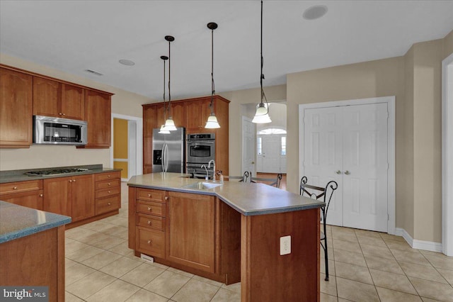 kitchen featuring light tile patterned flooring, stainless steel appliances, pendant lighting, and an island with sink