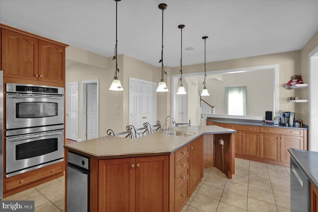 kitchen with sink, double oven, an island with sink, and decorative light fixtures