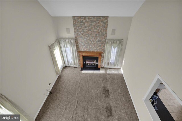 unfurnished living room with light carpet, a stone fireplace, a towering ceiling, and plenty of natural light