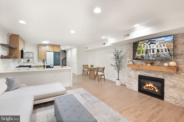 living area with recessed lighting, crown molding, light wood finished floors, and a fireplace