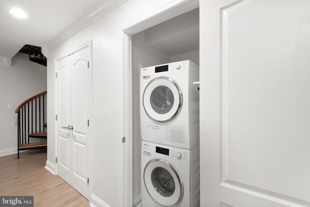 clothes washing area featuring light hardwood / wood-style floors, stacked washing maching and dryer, and ornamental molding