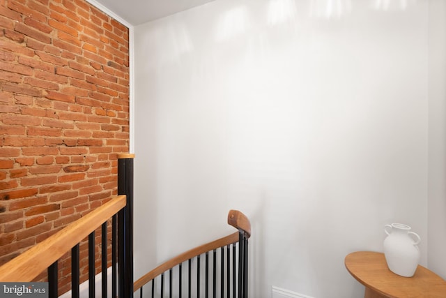 hallway with brick wall, baseboards, and an upstairs landing