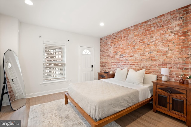 bedroom featuring recessed lighting, wood finished floors, baseboards, and brick wall