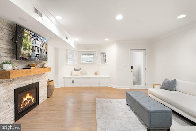 living room featuring crown molding, a stone fireplace, and light hardwood / wood-style floors