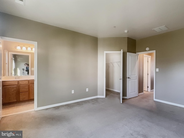 unfurnished bedroom with a spacious closet, sink, a closet, ensuite bath, and light colored carpet