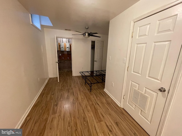 hall with wood finished floors, visible vents, and baseboards