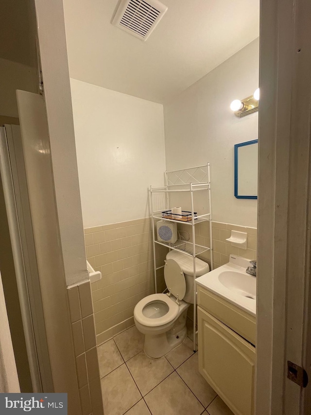 half bathroom featuring tile patterned floors, wainscoting, tile walls, toilet, and visible vents