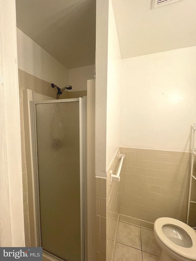 bathroom with a wainscoted wall, toilet, tile walls, a stall shower, and tile patterned flooring