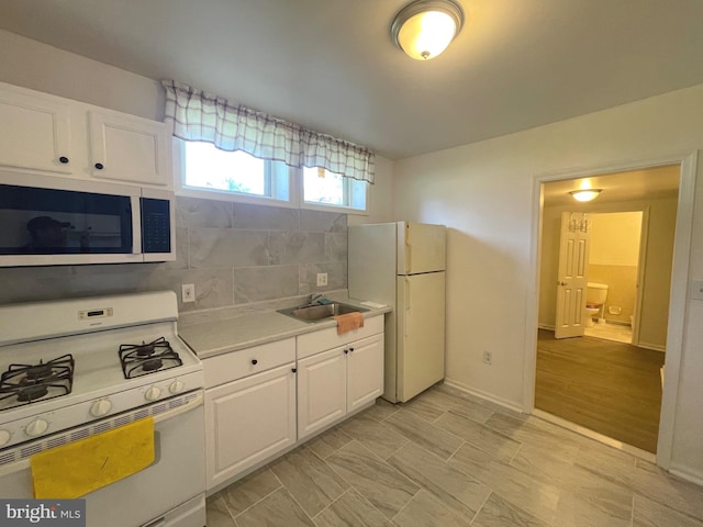 kitchen featuring a sink, backsplash, white cabinetry, white appliances, and light countertops
