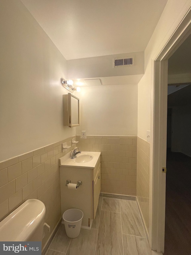 bathroom with vanity, toilet, and tile walls