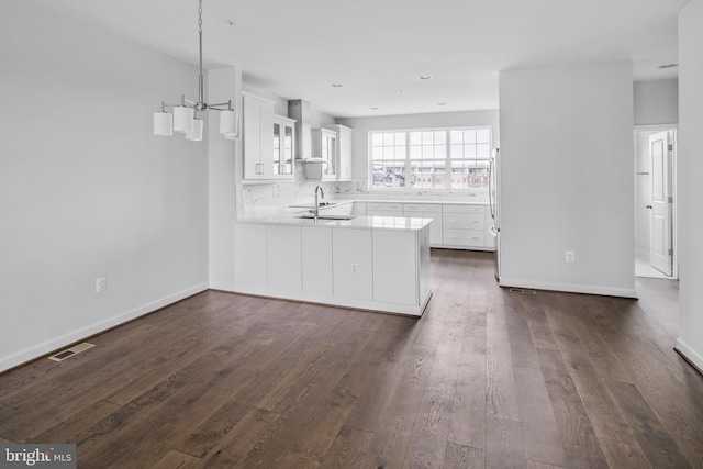 kitchen with kitchen peninsula, white cabinetry, sink, and wall chimney exhaust hood