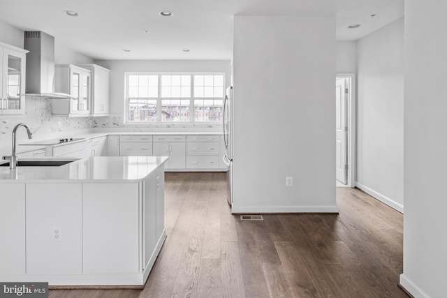 kitchen with wall chimney range hood, sink, dark hardwood / wood-style flooring, white cabinets, and stainless steel refrigerator