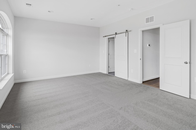 unfurnished bedroom featuring a barn door and dark carpet