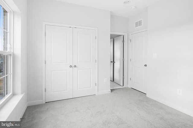 unfurnished bedroom with a closet, light carpet, and multiple windows